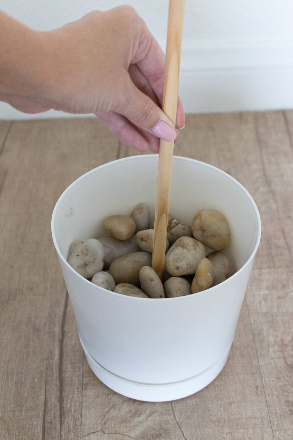 A person putting a stick in a cup of rocks.