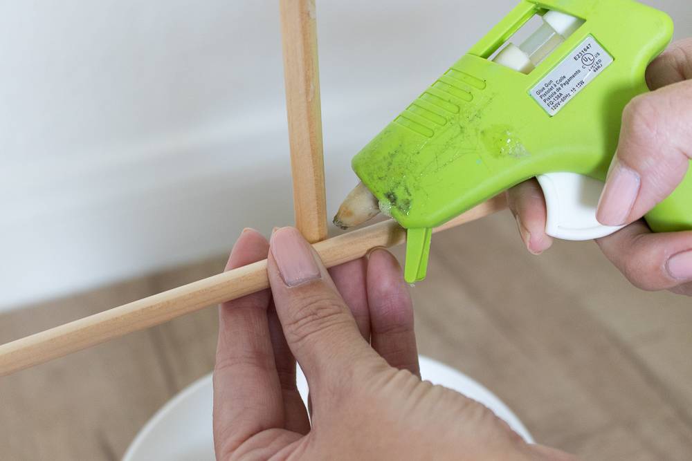A person using a green glue gun on two dowel rods.