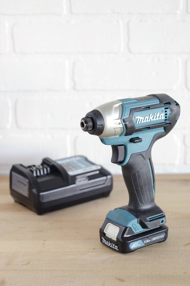 A cordless drill sitting beside the charger that charges it.