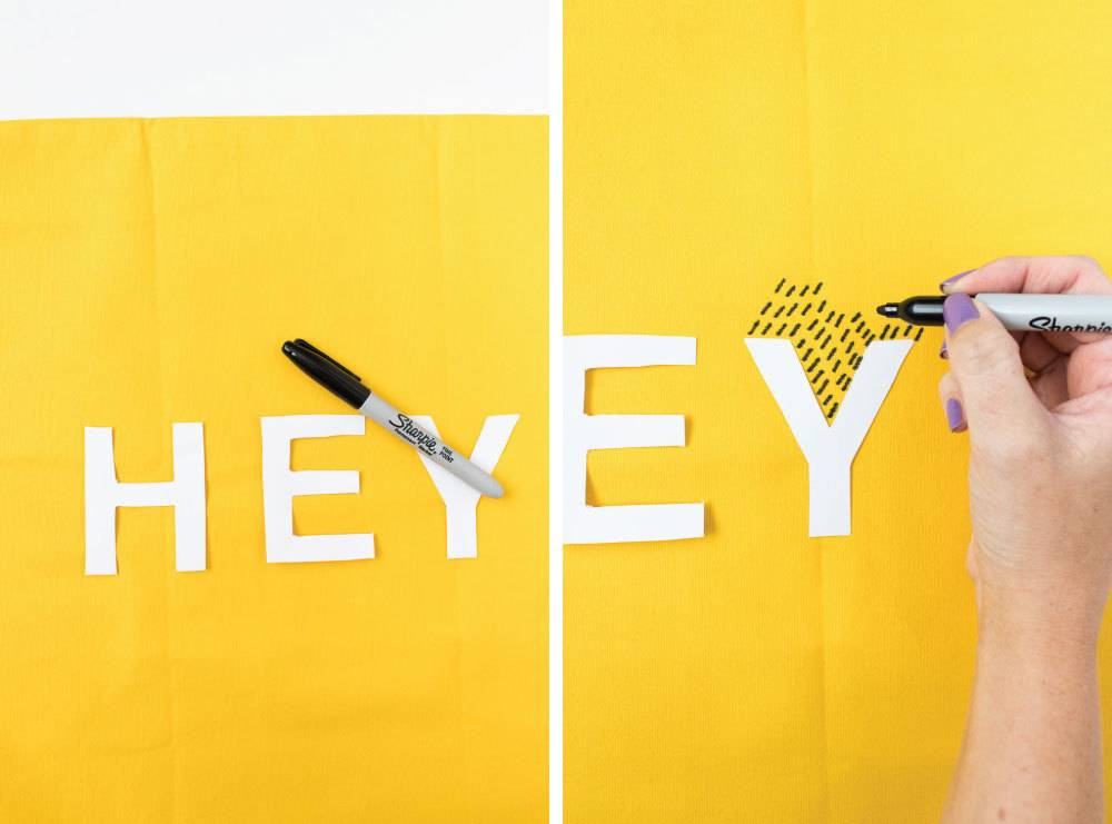A person using a marker on a yellow background with white letters.