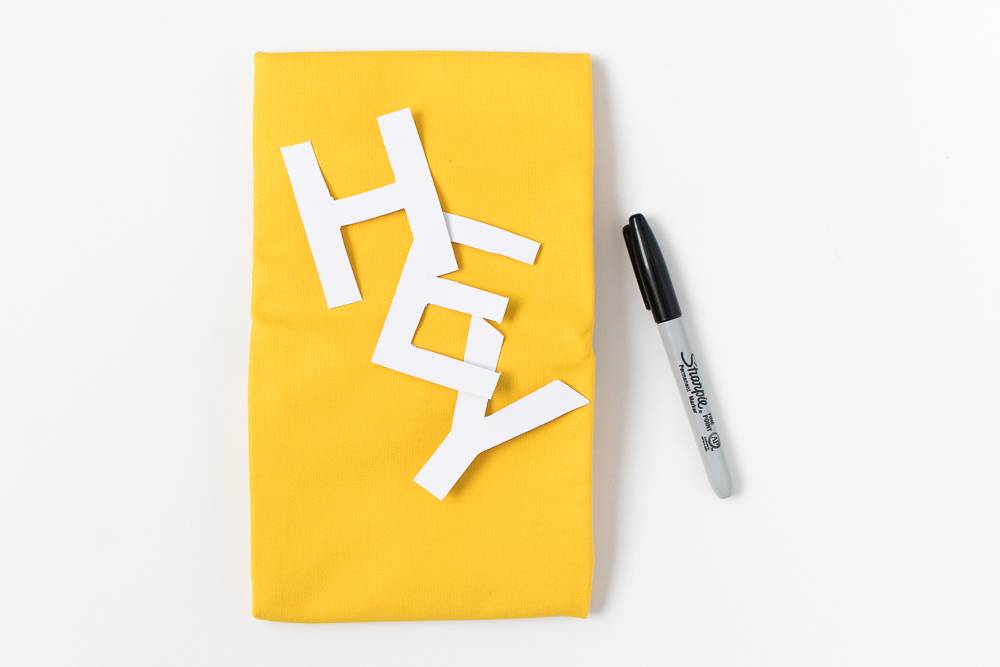Cut out letters are on a yellow sheet of paper, with a black pen.