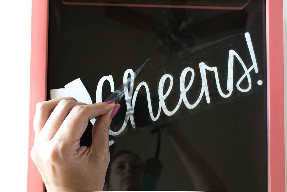 Woman removing transfer tape to reveal a word applied to a picture frame.