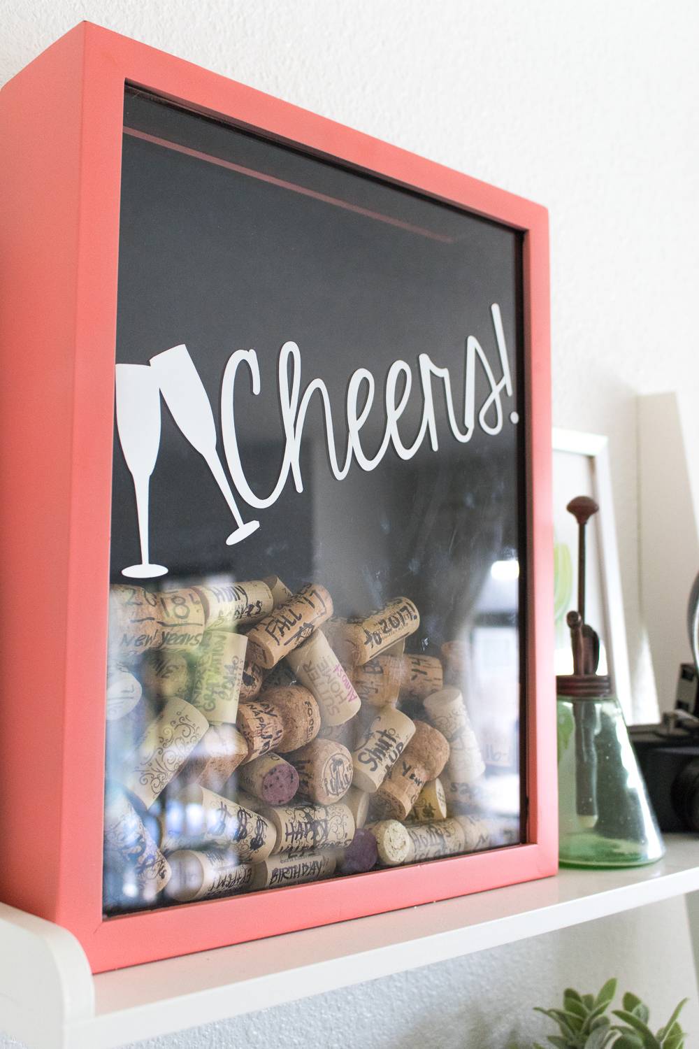 Corks are put into a red framed box with the word cheers on it.