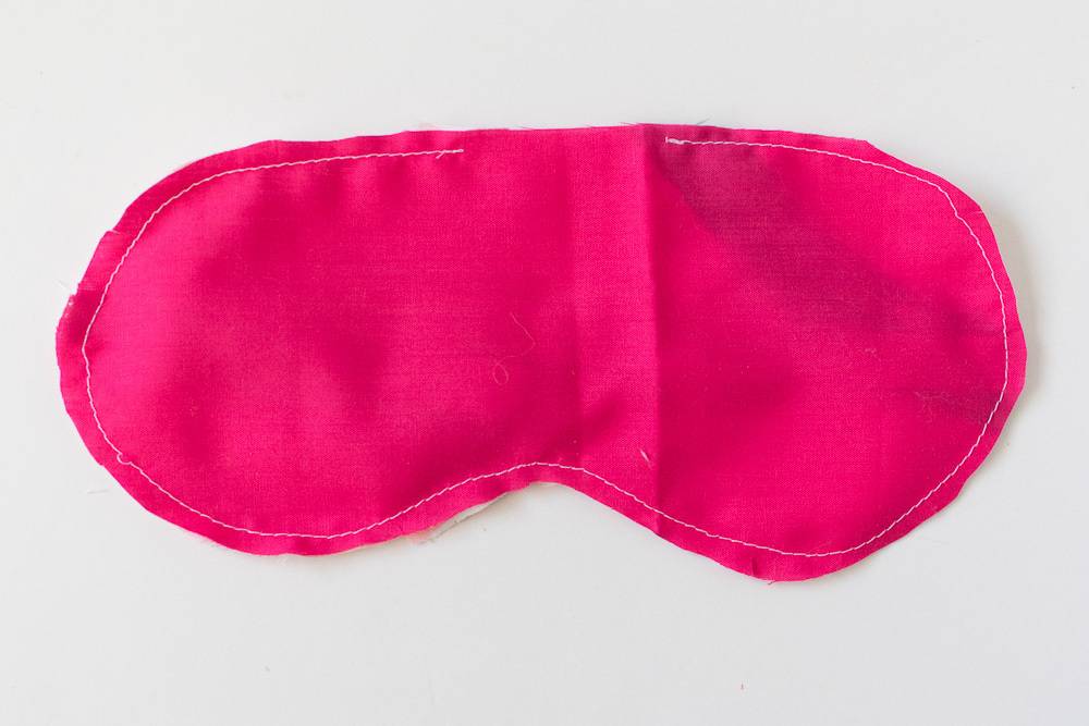 A pink fabric eye mask hand sewn with white thread.
