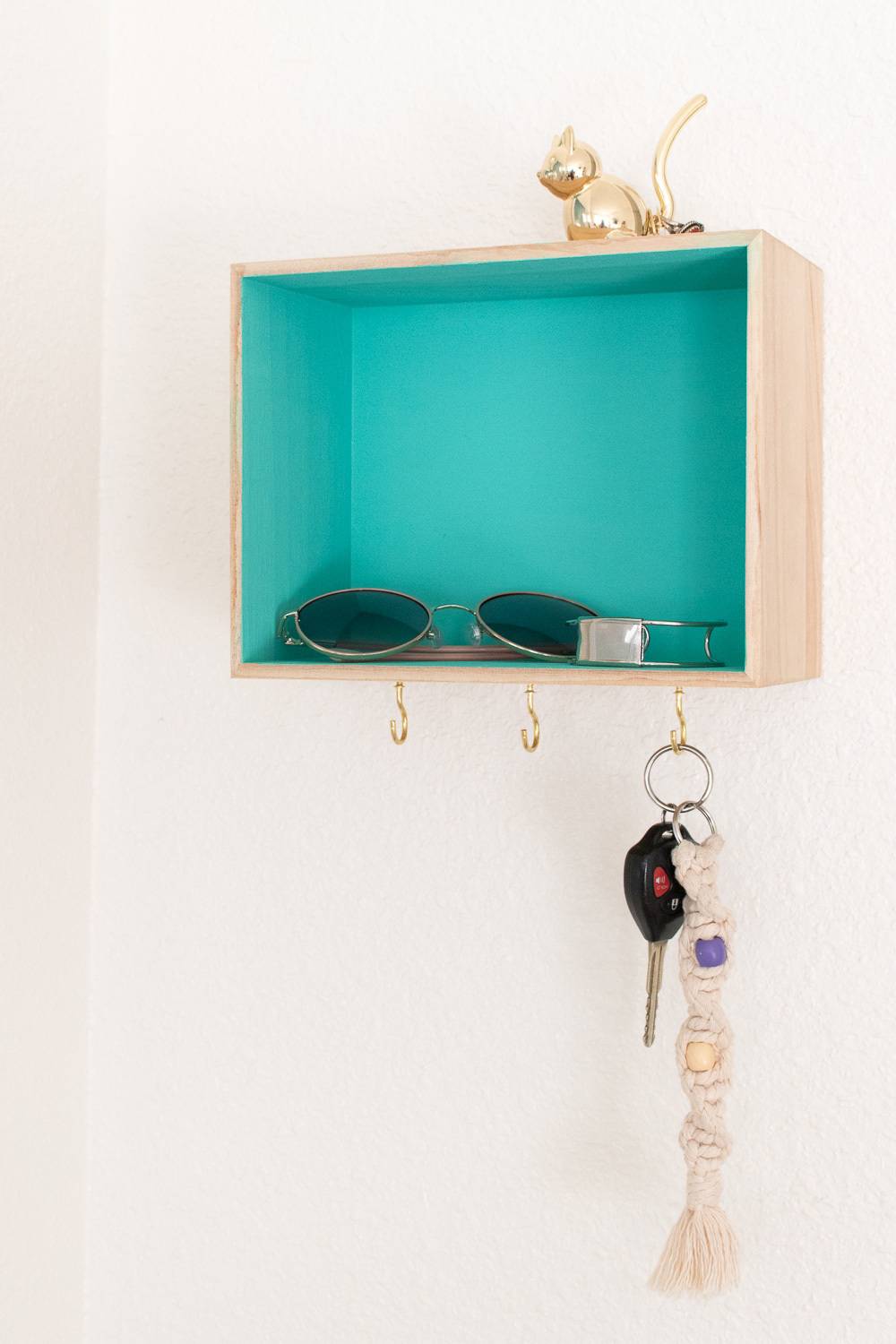 Open-front box shaped key organizer with hooks and aqua-blue interior, to hang on the wall.