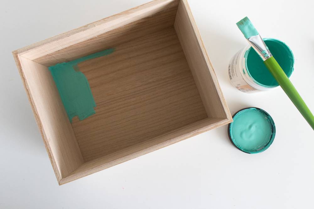 Wooden crate next to an opened jar of turquoise paint.