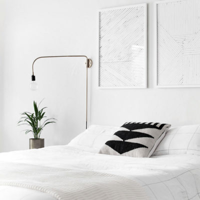 A bedroom has all white walls and an all white bed with a small plant in the corner.