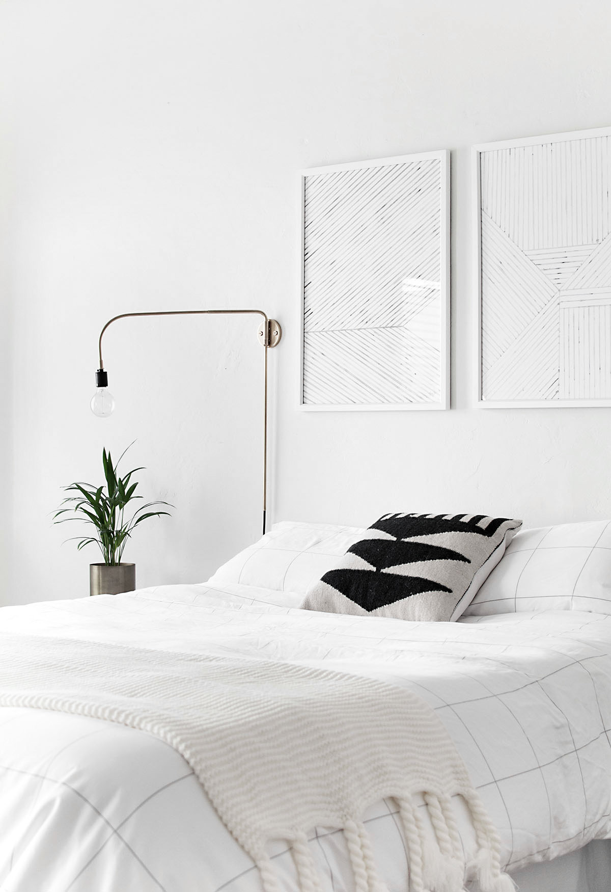 A bedroom has all white walls and an all white bed with a small plant in the corner.