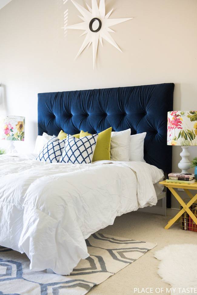 Large bed with a white comforter and navy blue tufted headboard in a bedroom.