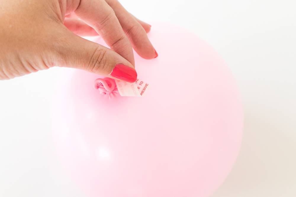 A woman placing tape on a pink balloon.