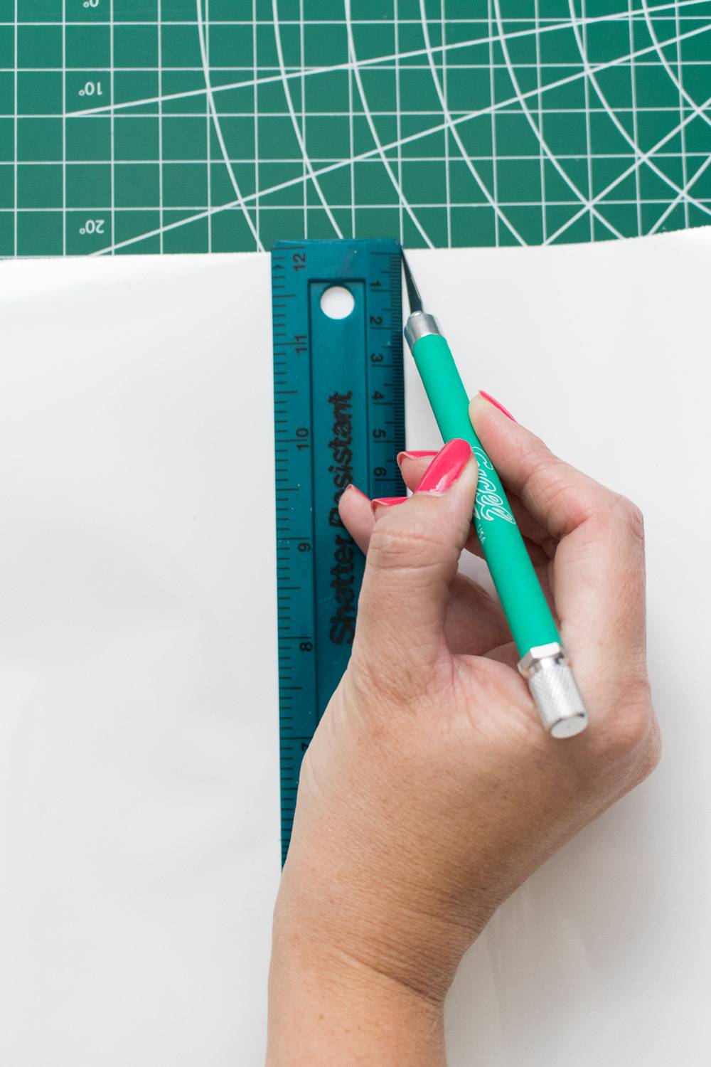 A person using a ruler and a pen knife on a board