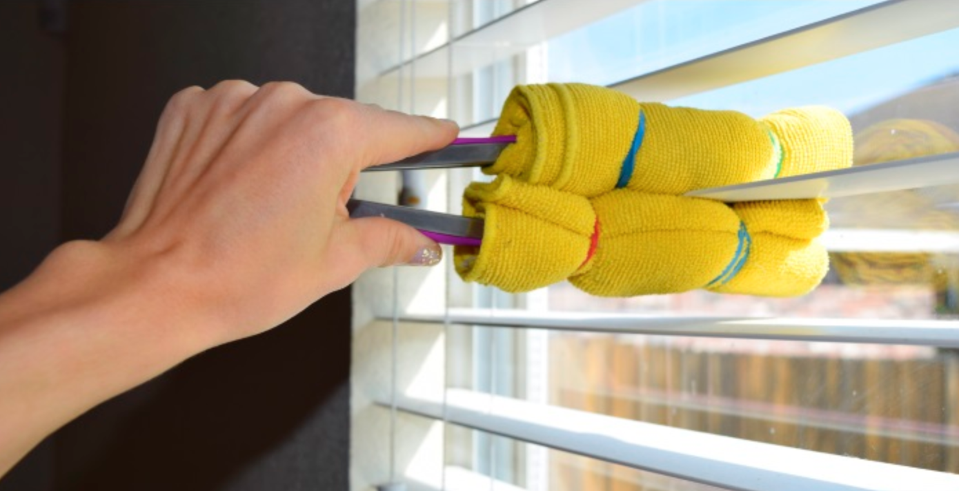 A person is using a tool with a yellow rag to clean a set of blinds.