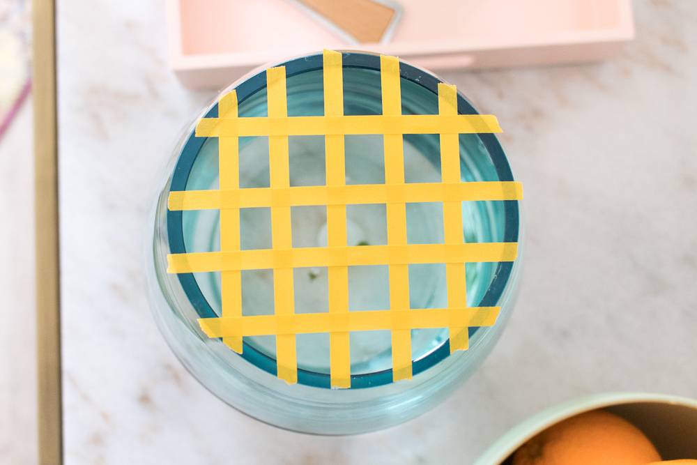 A small transparent blue glass object has yellow paper strung across it in a cross pattern.