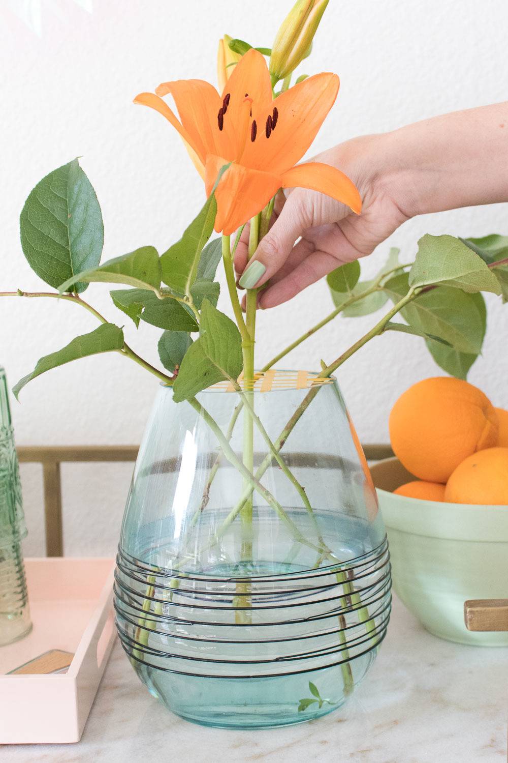 A person is putting an orange flower in a clear light blue vase.