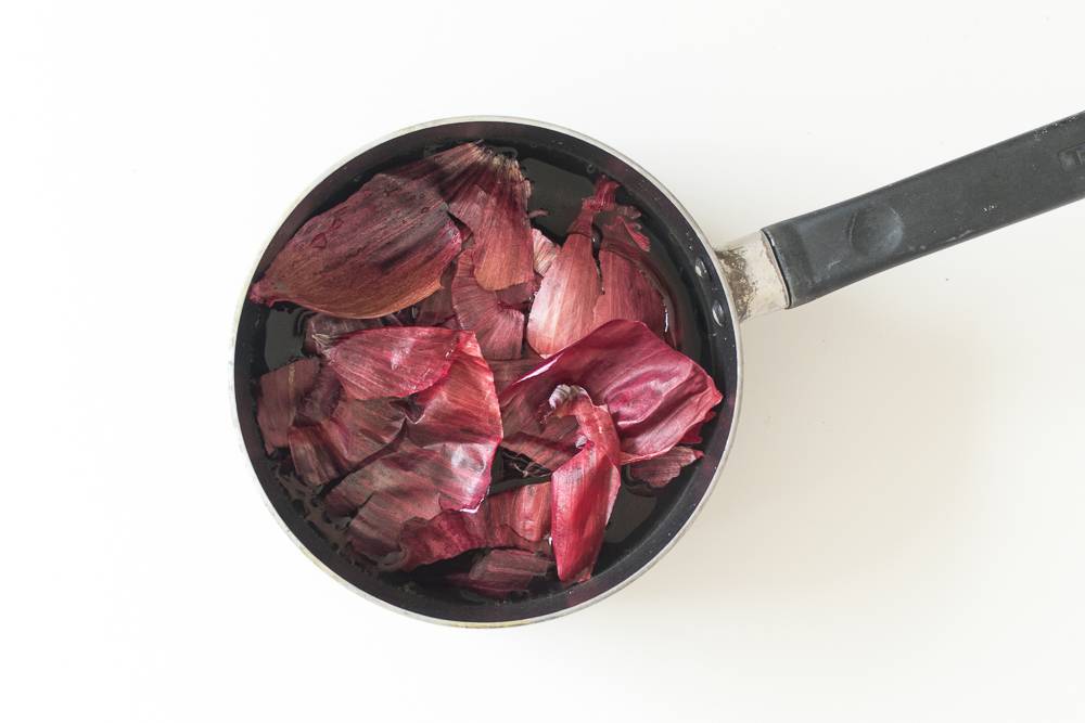 A slightly old pan with with some water and a lot of red onion peels.