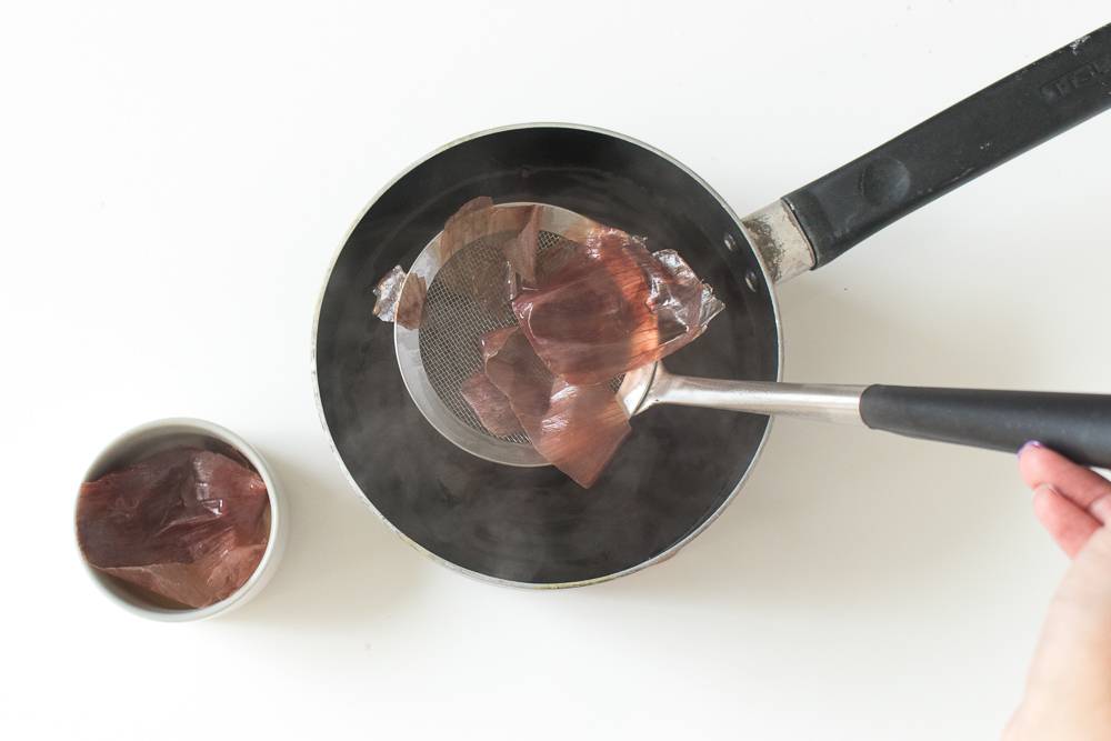 A person scooping gelatin out of a hot pan with a long silver and black ladle.