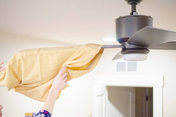 Woman is cleaning a wall ceiling fan with a cloth.