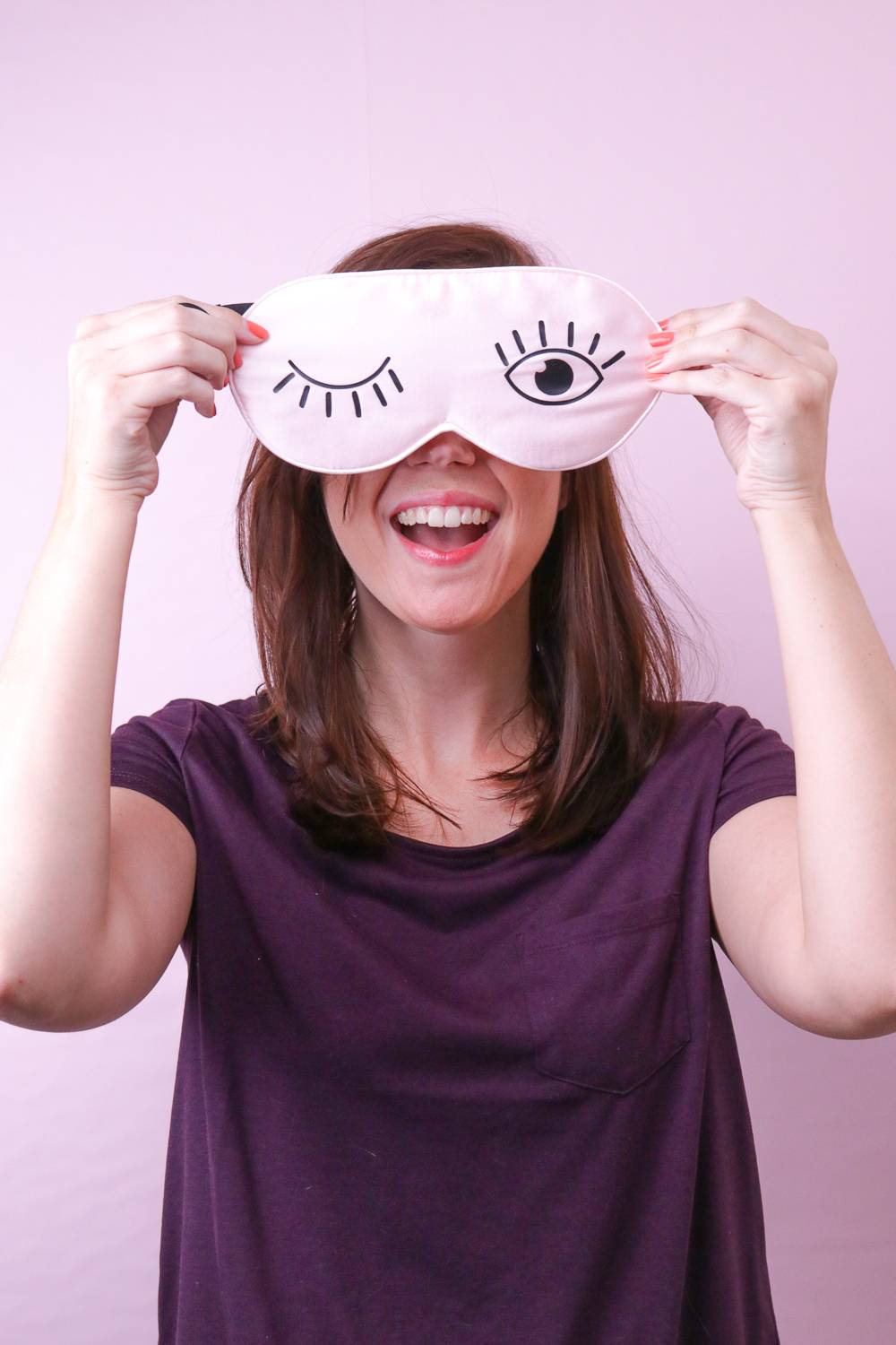 A woman holding an eye mask over her face with an open and closed eye on it.