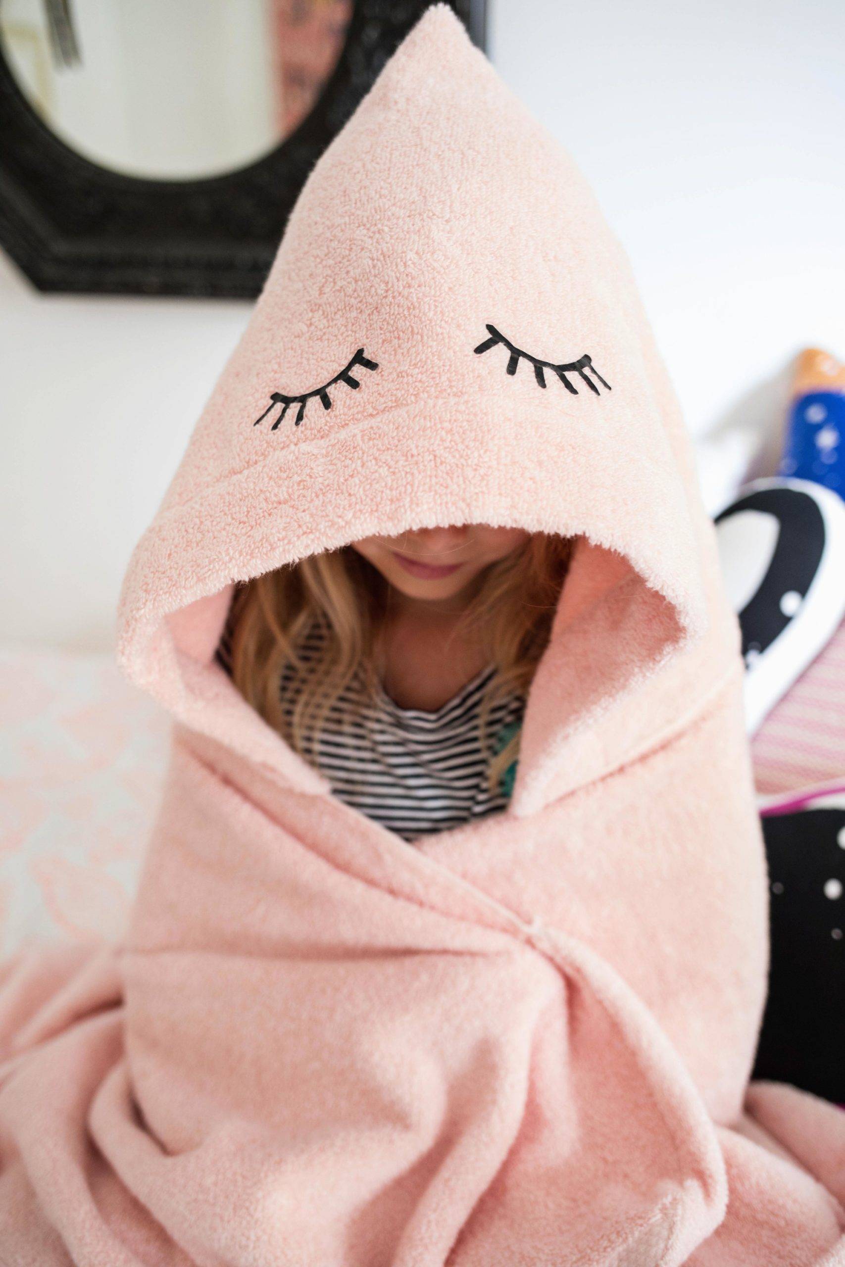 A girl is wrapped up in a pink towel with eyelashes on it.