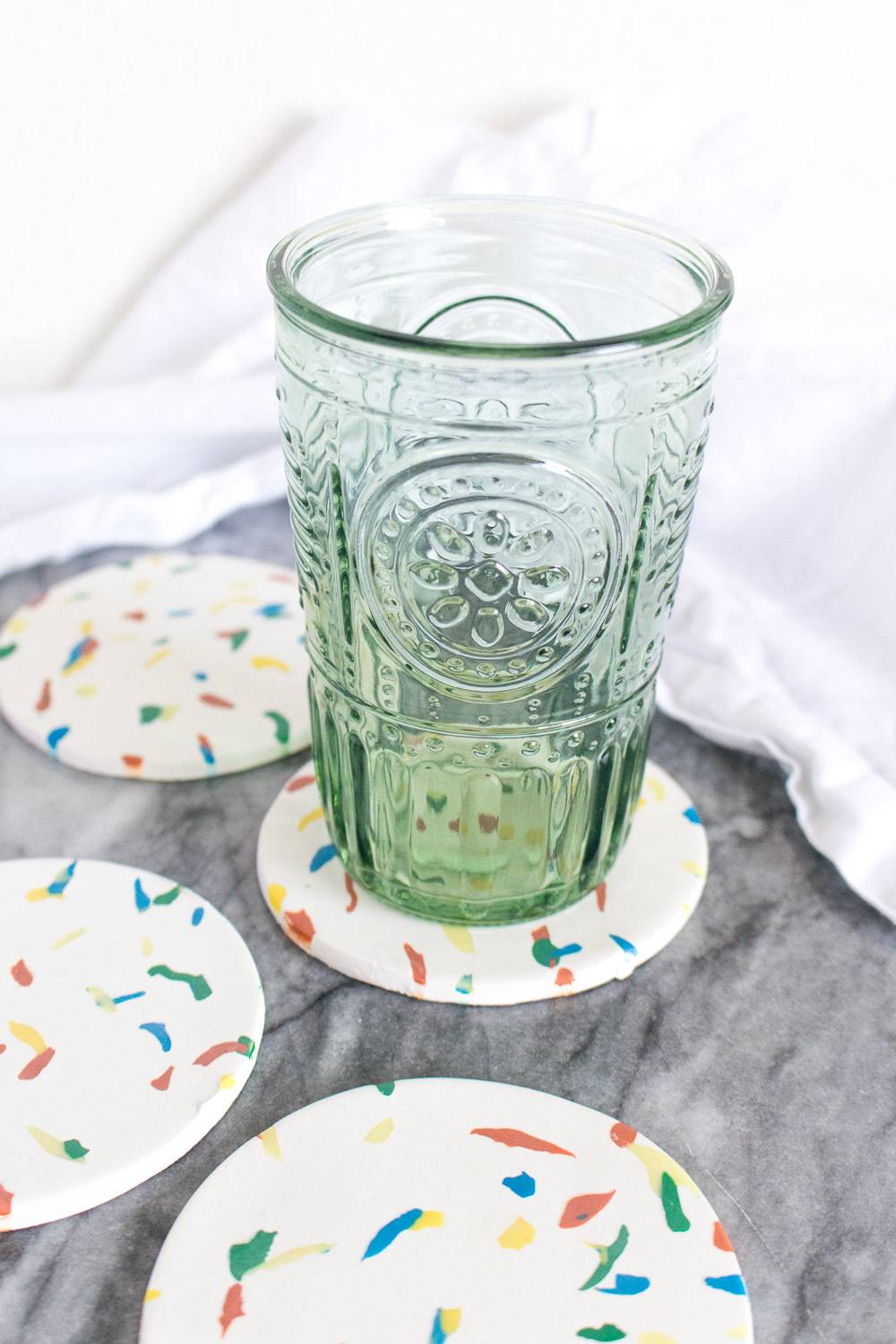 A clear glass is sitting on a white coaster with colorful dots.