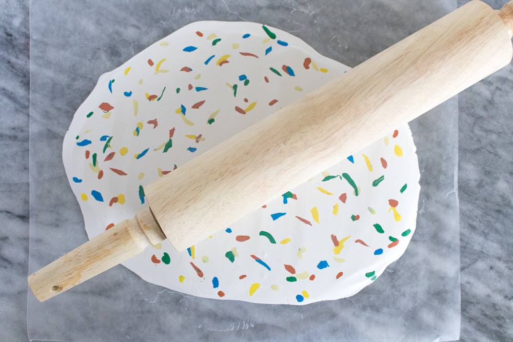 A wooden rolling pin laying on a multi colored rolled out dough on a grey marble surface.