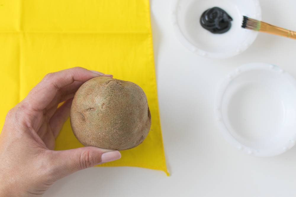 Hand holding a potato over yellow paper with two small bowls nearby.
