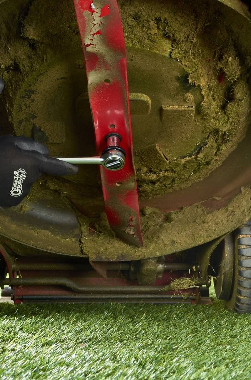 The underside of a lawnmower with a red blade and caked grass around the edges.