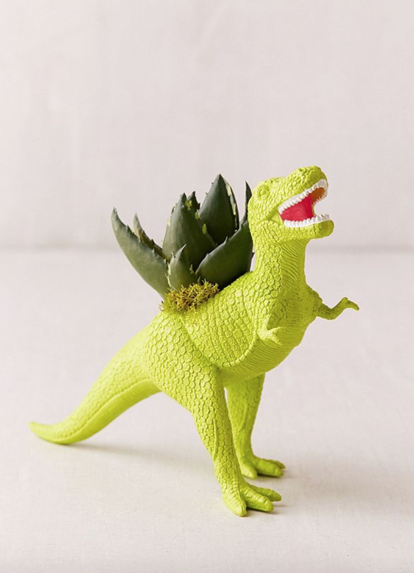 A green plastic dinosaur is standing on a white surface.