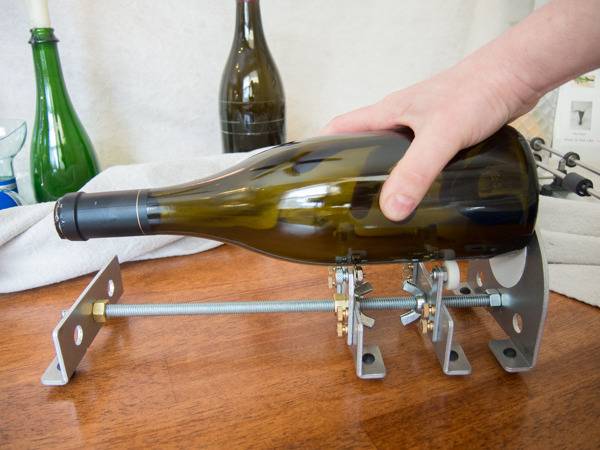 Holding a glass wine bottle over a bote cutter.