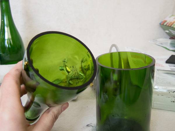 A hand holds the top part of a green glass bottle that has been cut in half.