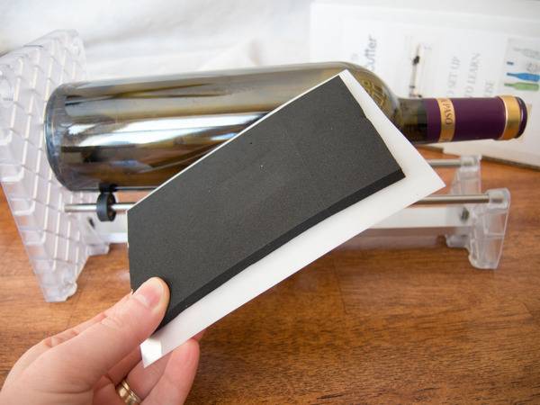 A hand holding a piece of paper and a glass bottle is lying near it.