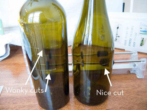 Two olive green wine bottles sit next to each other on a wooden table.