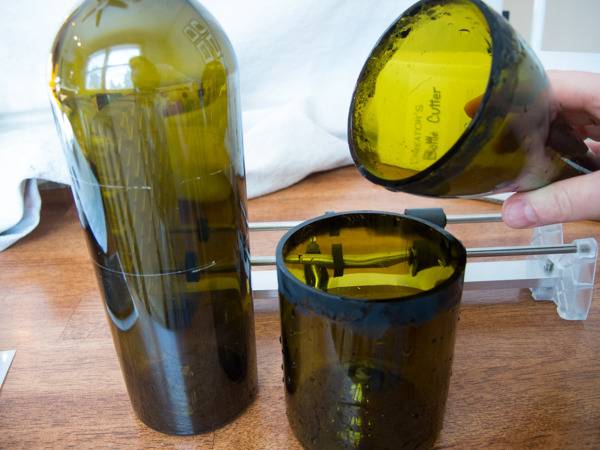 A hand holding top part of a glass bottle while the bottom part is lying near another glass bottle.