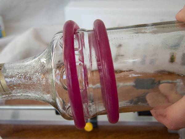 A glass bottle turned horizontal with two fuschia rings on it.