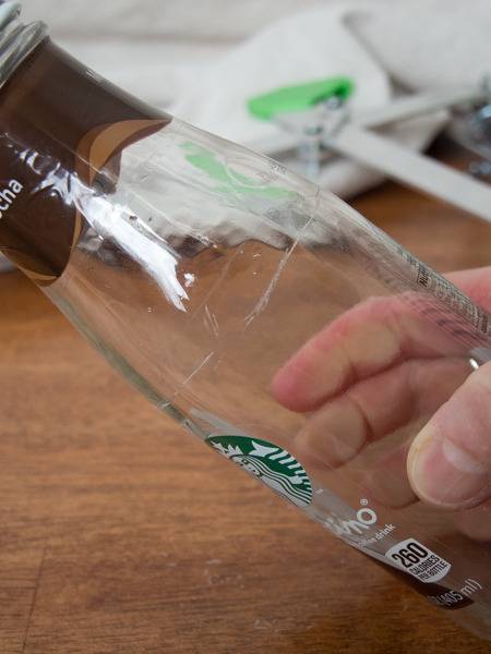 A glass Starbucks bottle held in a hand atop a wooden surface.