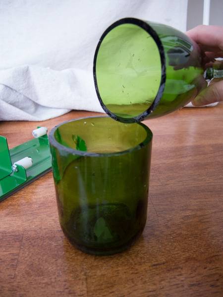 A person is pouring liquid from one green glass into another.