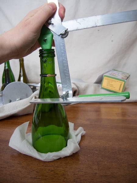 The top half of a green liquor bottle with a silver tool attached to the neck.