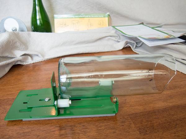 Cut bottle positioned horizontally in a green bottle cutter that sits on a wooden surface.