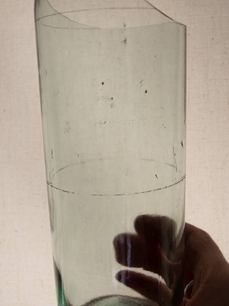 Hand holding a clear glass bottle with score mark around the center and the top already cut off.