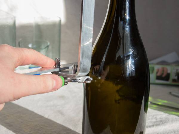 A hand is holding a contraption next to a dark wine bottle.