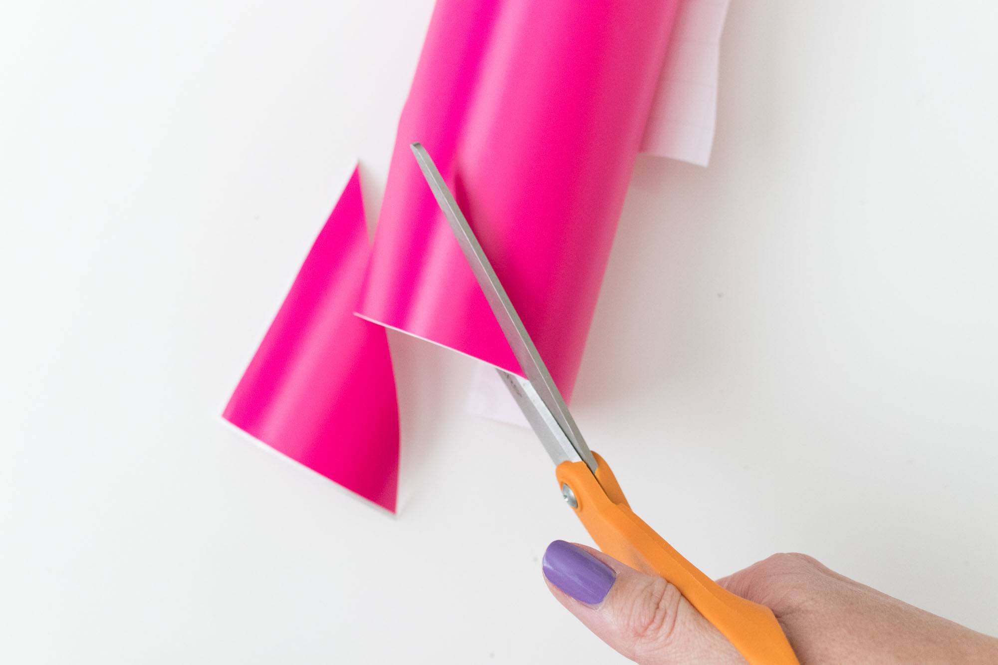 A female hand cutting pink paper with a pair of scissors.