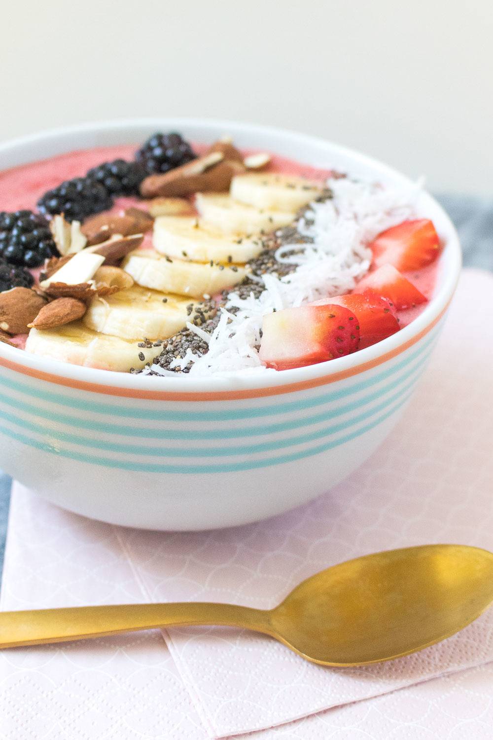 A golden spoon next to a smoothie bowl with fruit and other toppings.