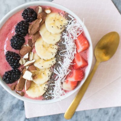 A large bowl of porridge with fruit in it next to a brown spoon