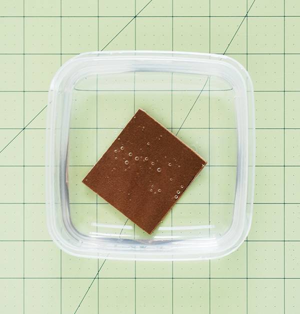 A brown square item set in a clear container on a sheet of paper.