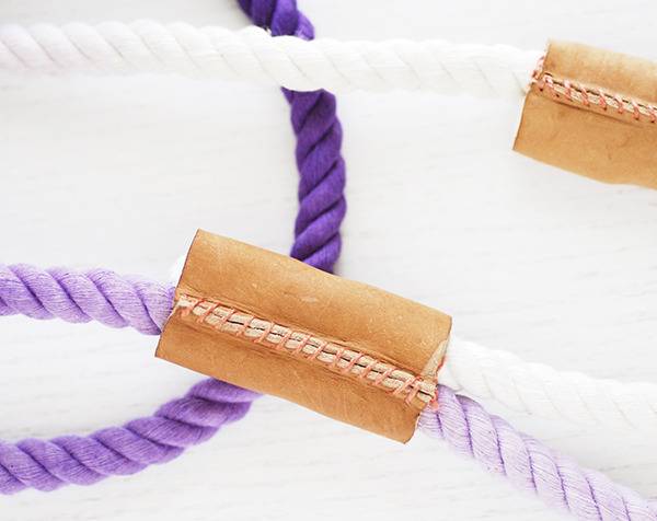 A purple and a white piece of rope coming together under a piece of sewed leather.