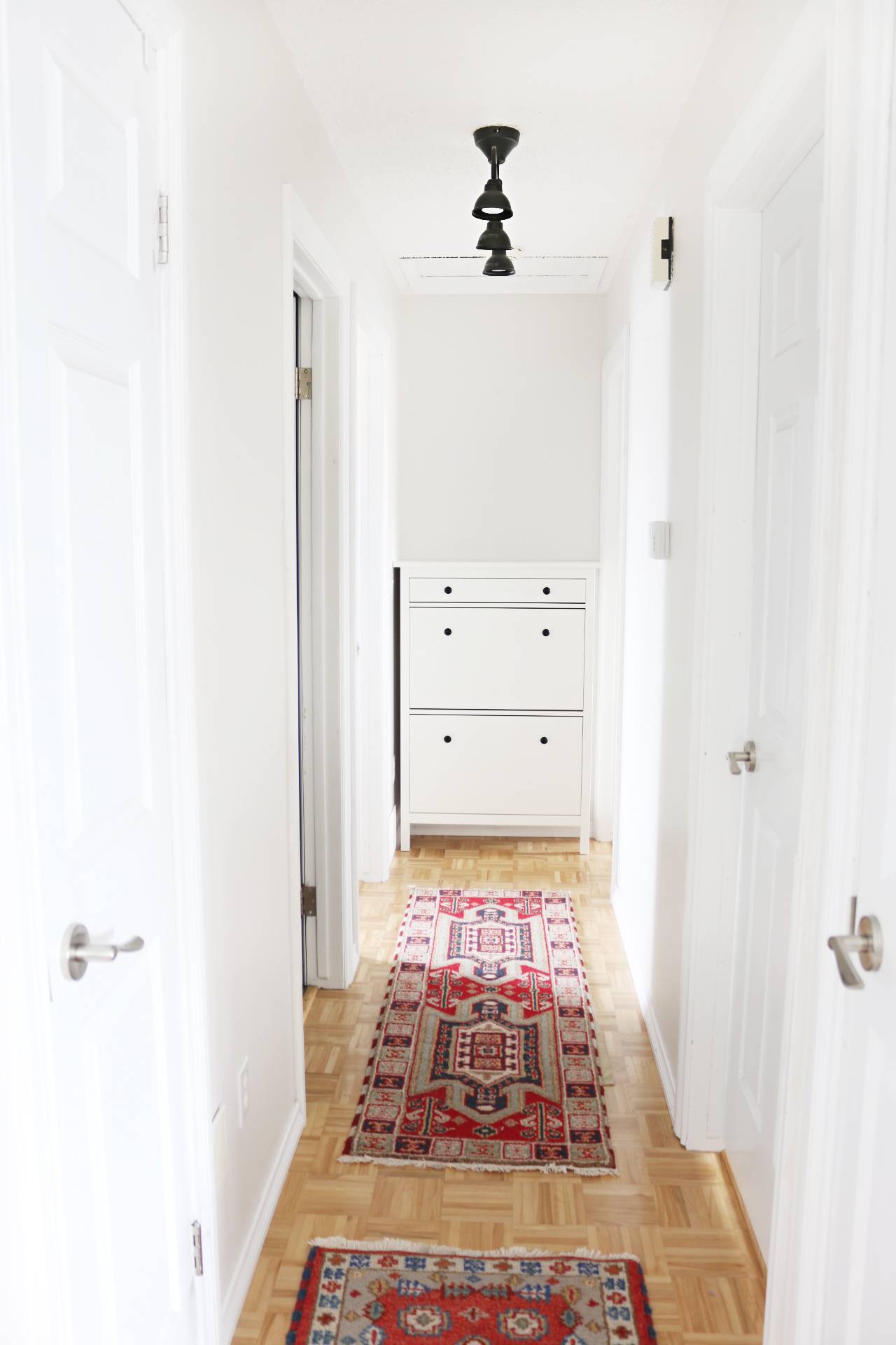 Two red rugs sitting on a floor in a hallway with white walls.