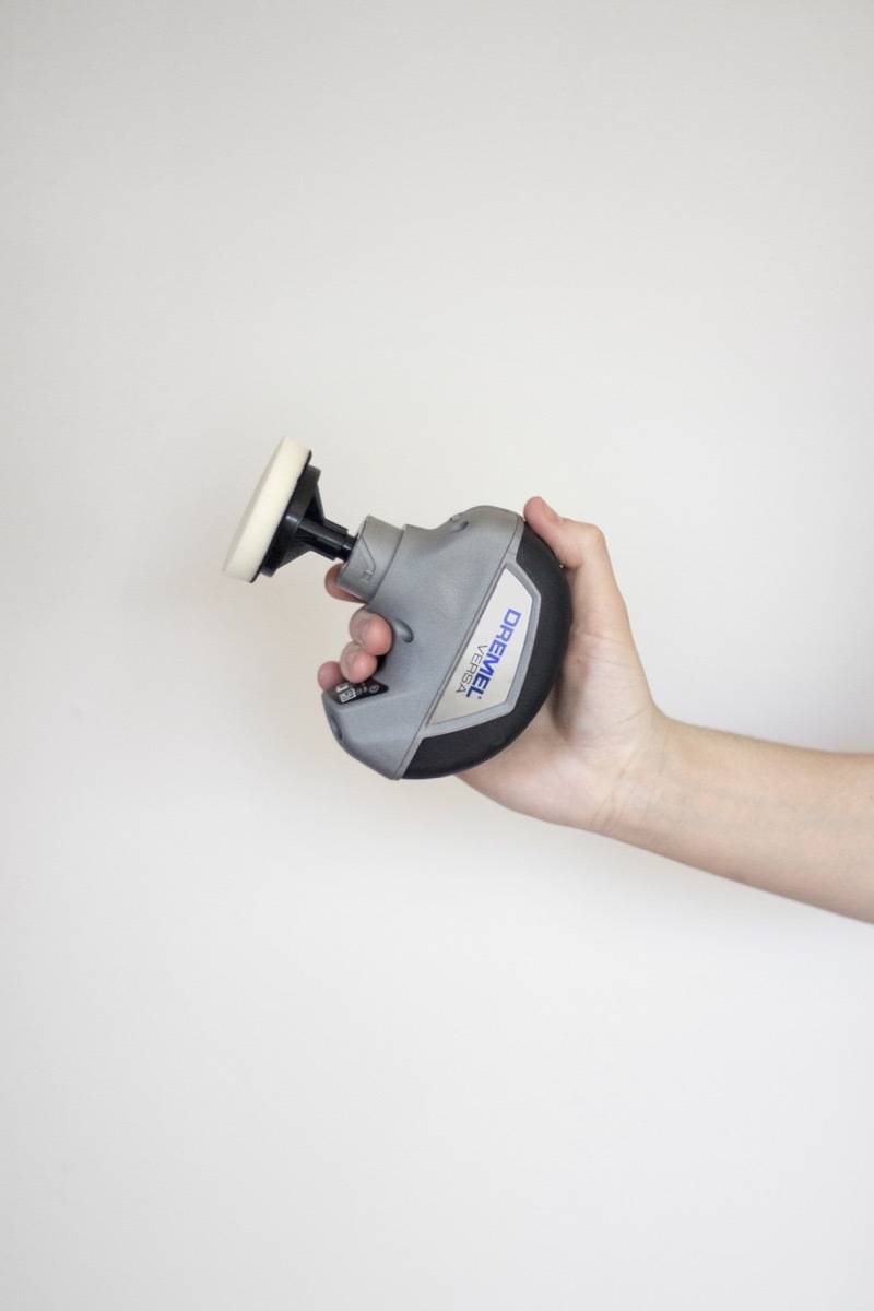 Person holding a small silver handled tool with a white top against a white wall.