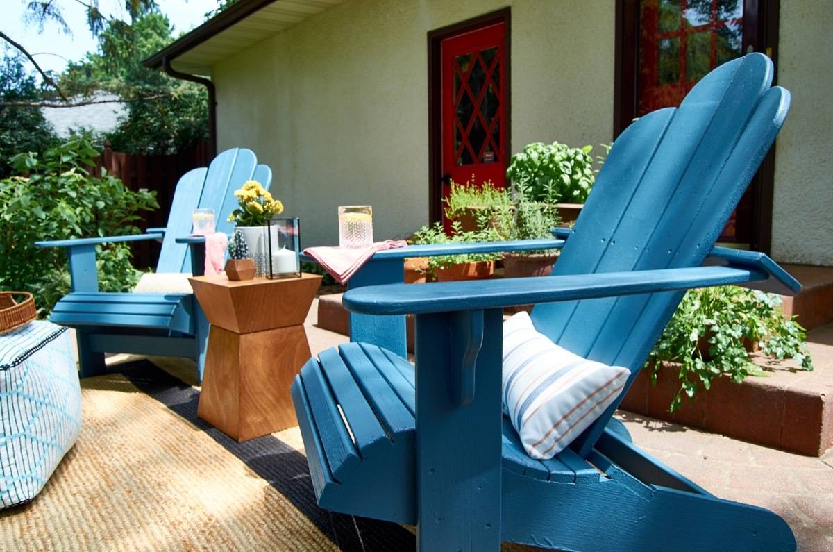 Outdoor patio with two blue chairs and white throw pillows nestled between a modern wood end table.