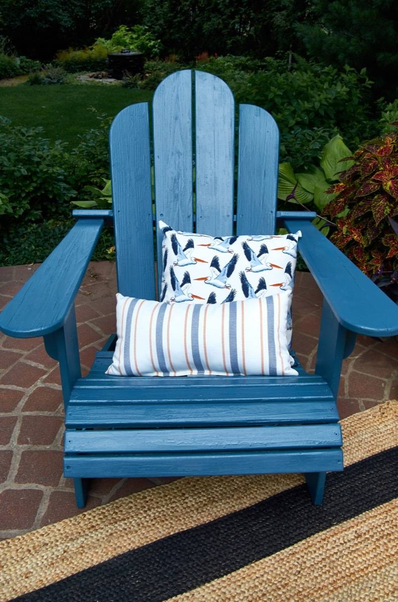 A blue lawn chair on a rug and stones with pillows on it.