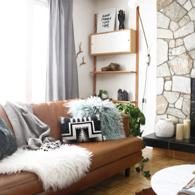 A brown couch with a white furry throw and a brown cowskin rug in a living room.